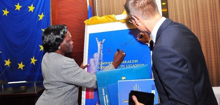 Minister Sarah Opendi and Mr. Thomas Tiedemann autograph a large format book cover print-out at the ceremony