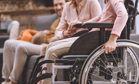 cropped shot of mother and daughter in wheelchair holding hands at home 