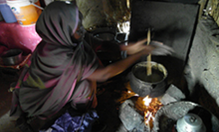 Photo of a woman cooking on a firewood stove.