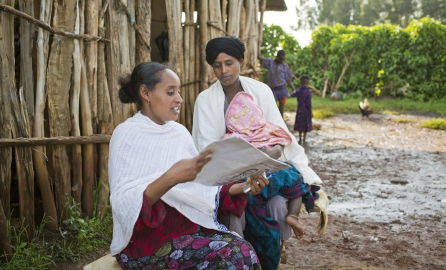 photograph of two women and a child in a village, with one reading an informational leaflet