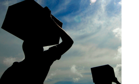 Backlit photograph of men carrying boxes on their heads
