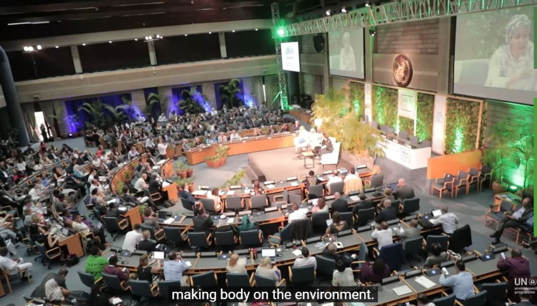 Vie of the UN Environment Assembly hall, hemisphere with delegates sitting behind desks, looking at the podium on the right where the President of the Assembly is speaking