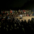 Large number of people sitting on ground watch projection on large screen