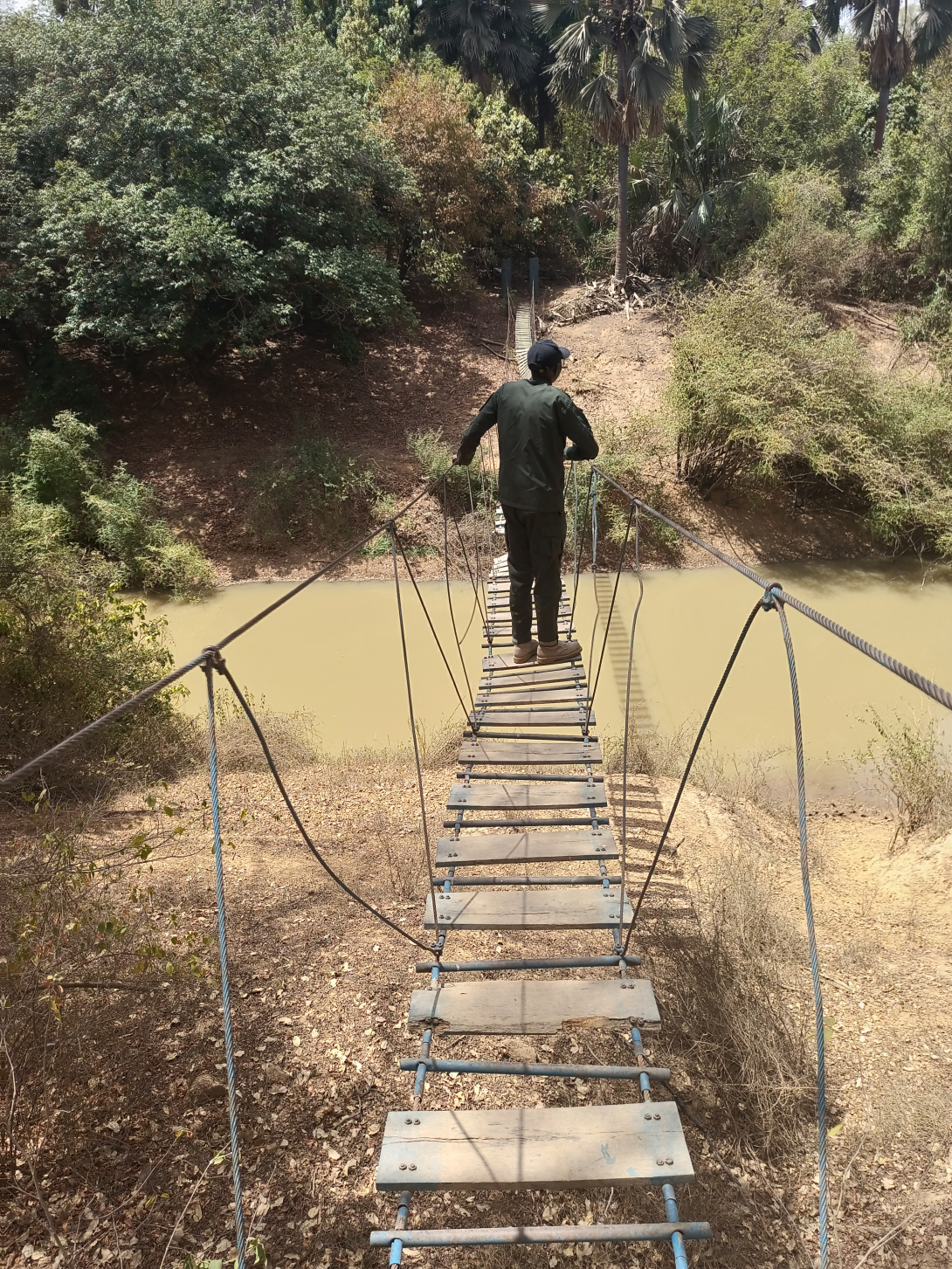 man walking on rope bridge over river in arid landscape